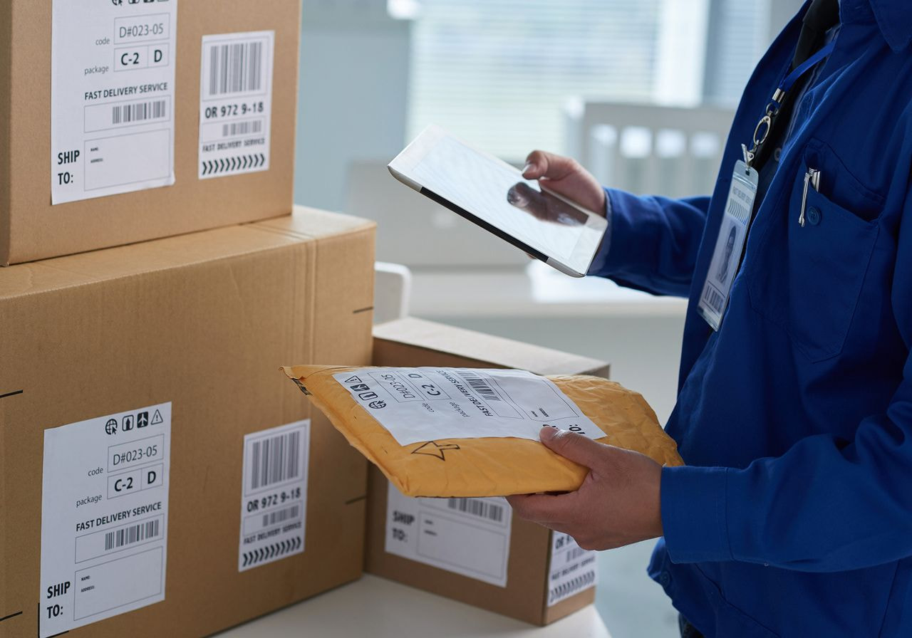 A man in a blue shirt holds a tablet while examining several boxes in front of him.