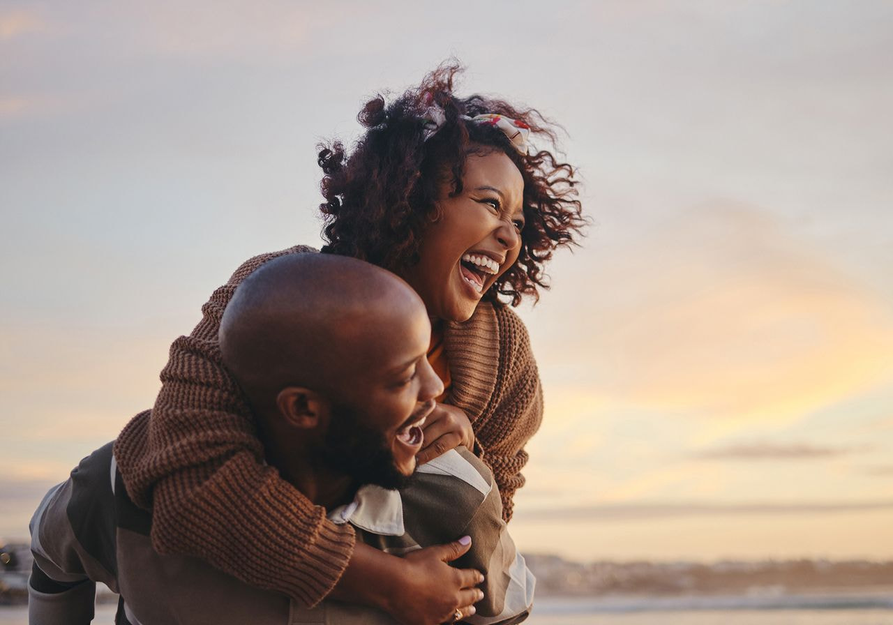A joyful couple at the beach during sunset, with the woman playfully piggybacking on the man.