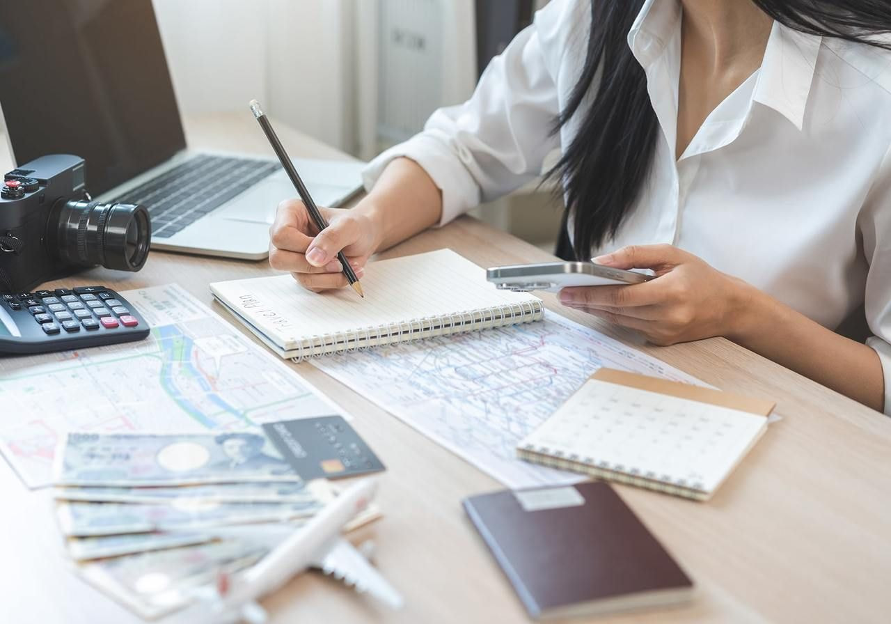 A woman sits at a desk, focused on her laptop, with a pen in hand, ready to take notes or write.
