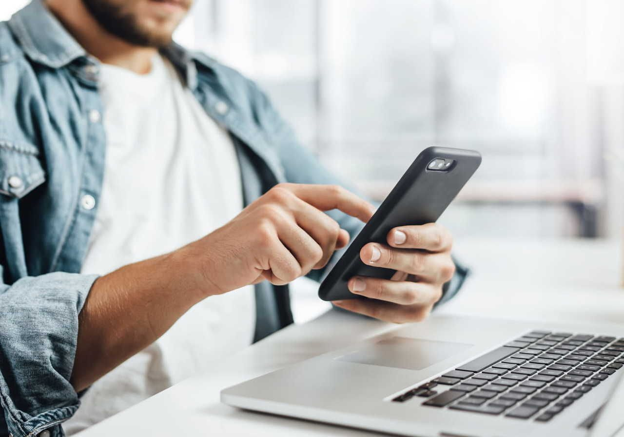 A man in glasses and a blue square shirt is making notes during an online class.