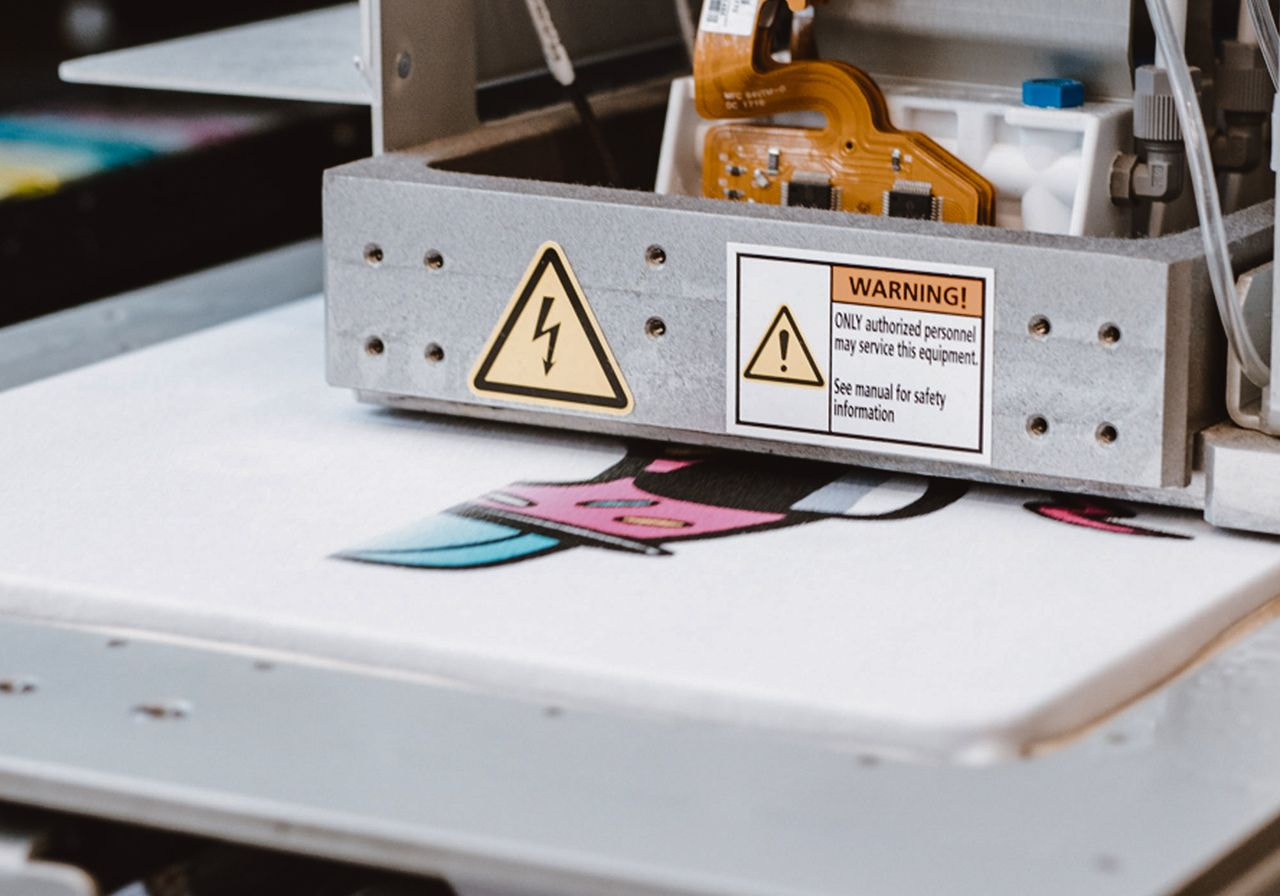 A close-up of a printing machine working on a colorful design, with warning signs visible on the machine.