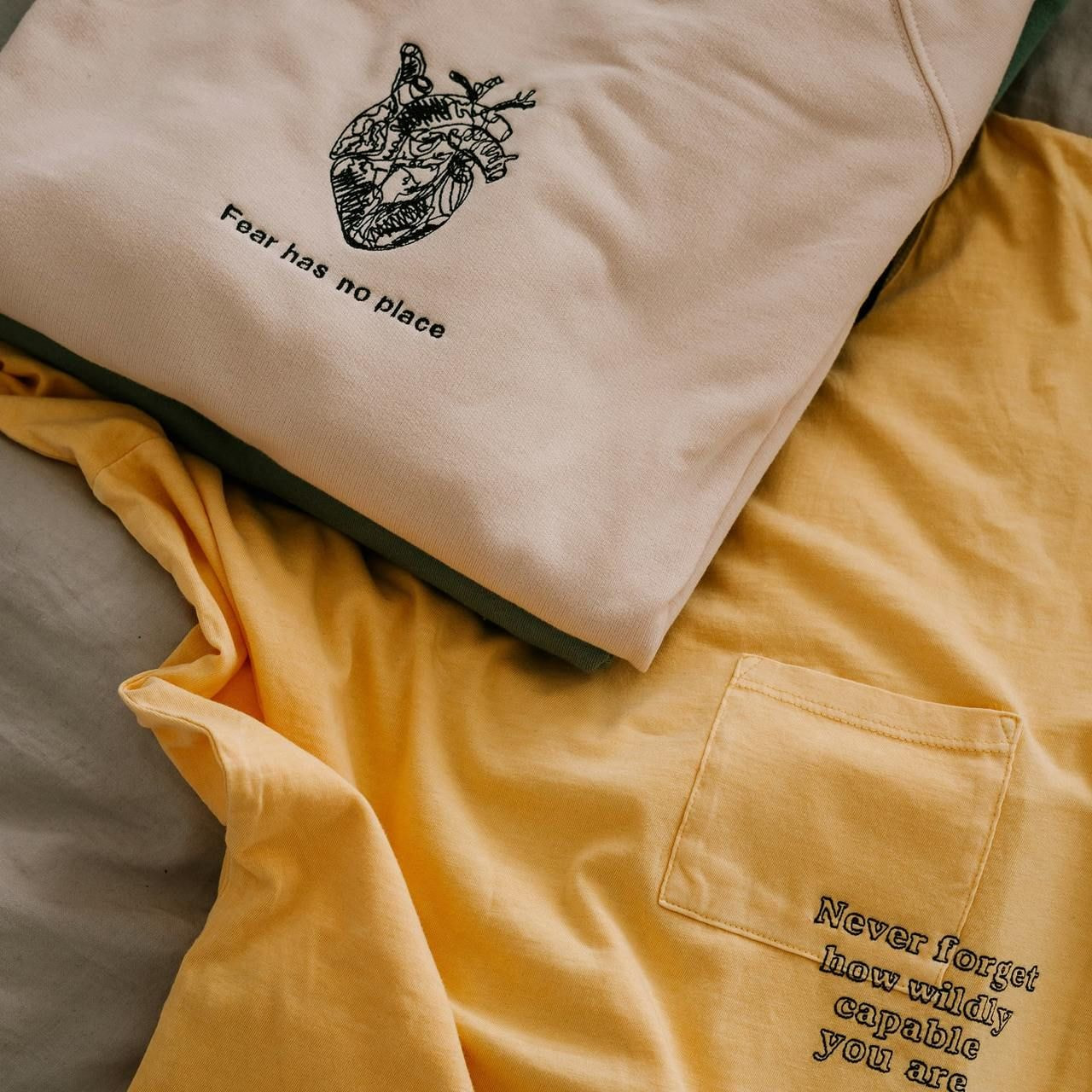 A yellow t-shirt with a heart design next to a green shirt featuring a similar heart graphic.