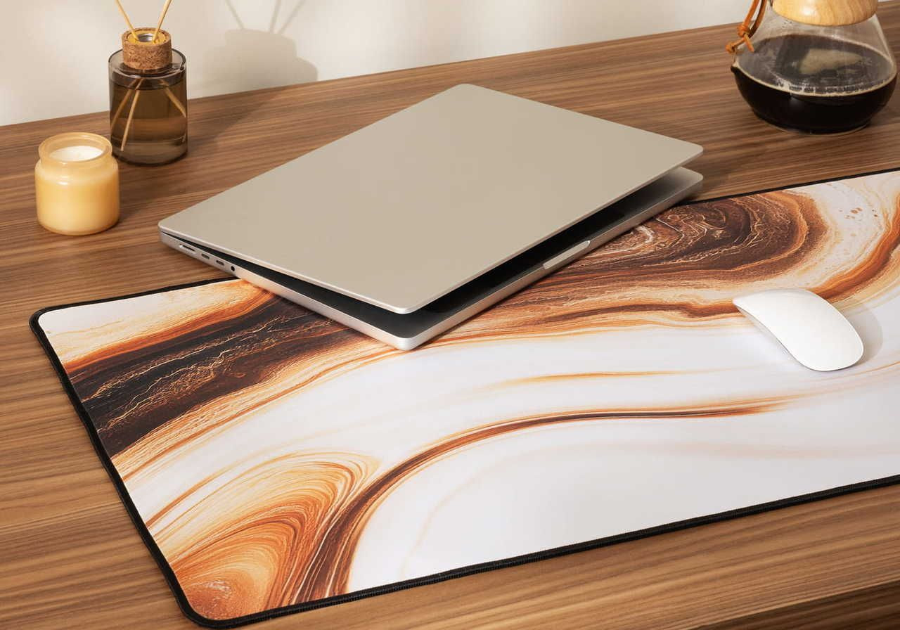A laptop and a white mouse on a stylized mouse pad with a marble design, placed on a wooden desk.