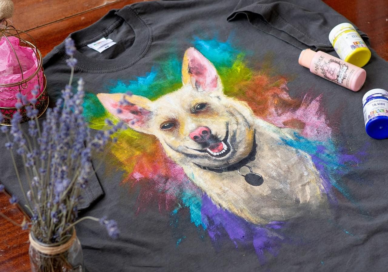 A t-shirt featuring a hand-painted dog, surrounded by paint and art supplies.