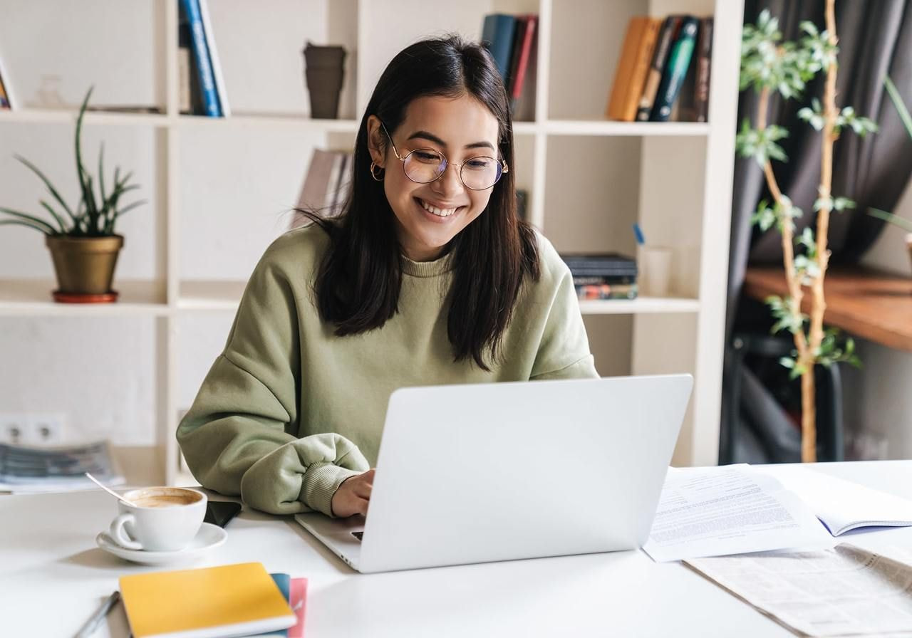 A woman smiles while working on her laptop, conveying a sense of joy and engagement in her task.