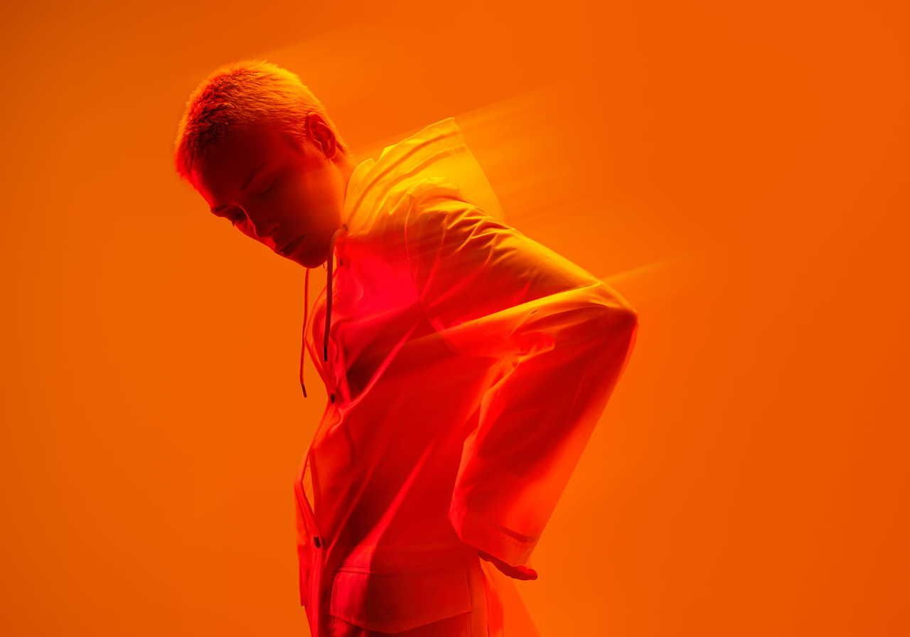 A cyberpunk fashion model with short hair wearing a white jacket poses against a vibrant orange background.