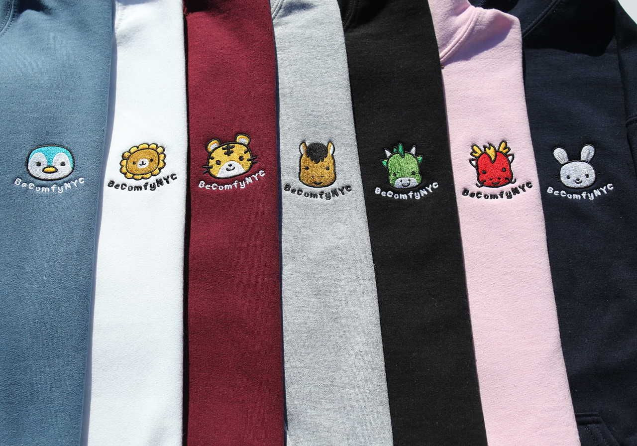 A row of hoodies in various colors, each featuring a cute embroidered character and the text "BeComfyNYC" on the chest.