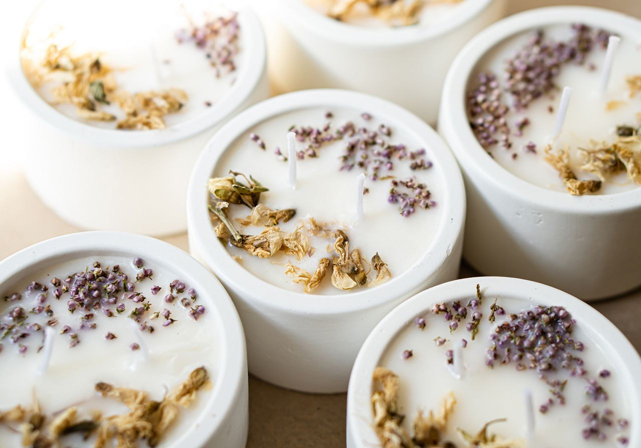 White ceramic candles topped with dried lavender and flower petals sit clustered together on a table.
