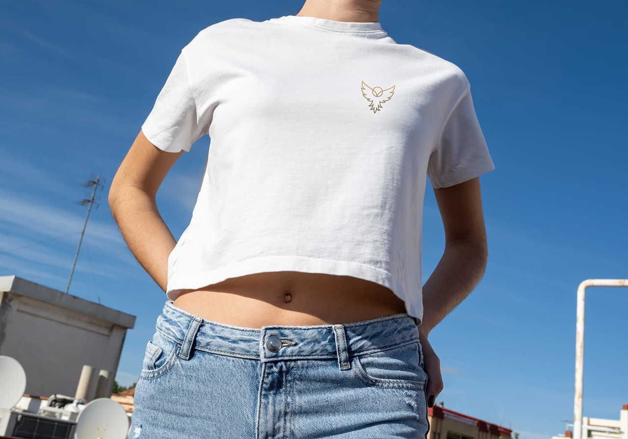 A person in a white crop top with a small eagle logo stands outside under a clear blue sky.