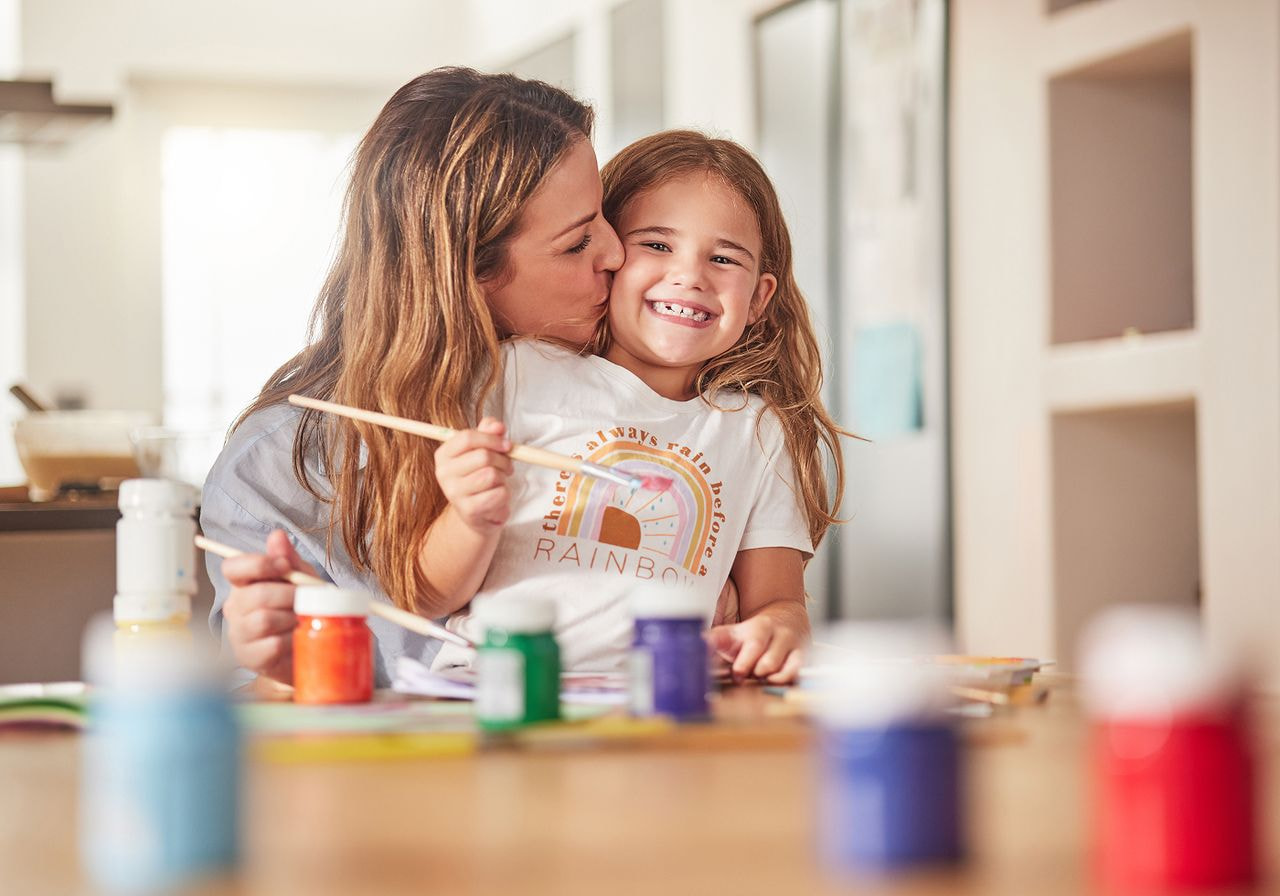 A woman and child sit at a table, surrounded by paint and brushes, engaged in a creative painting activity.