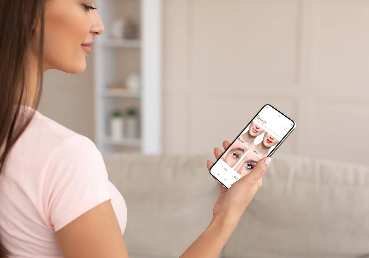 A woman holds a smartphone displaying a close-up image of her face, smiling at the camera.