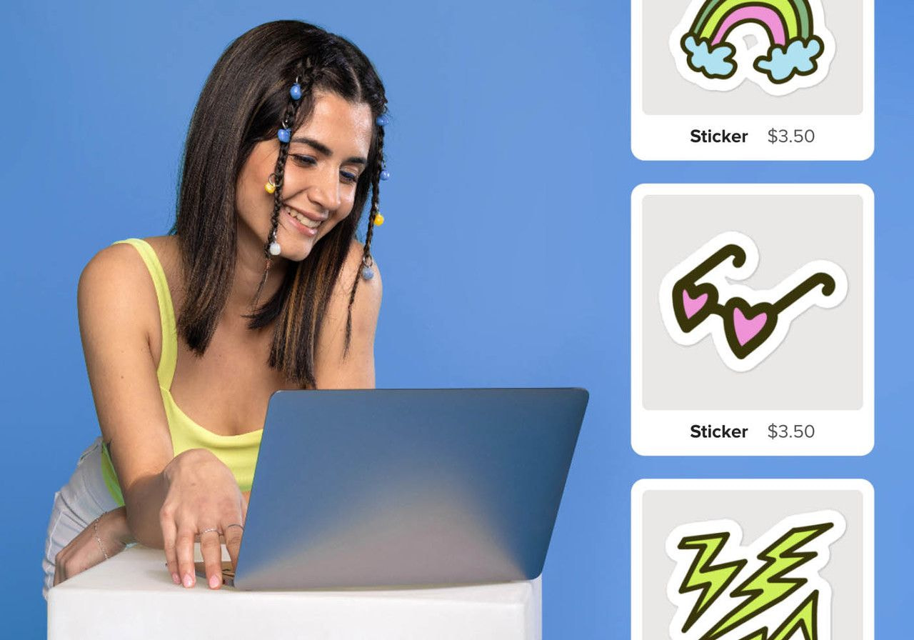 A woman with braided hair adorned with beads sits smiling at a laptop. Beside her are colorful stickers.
