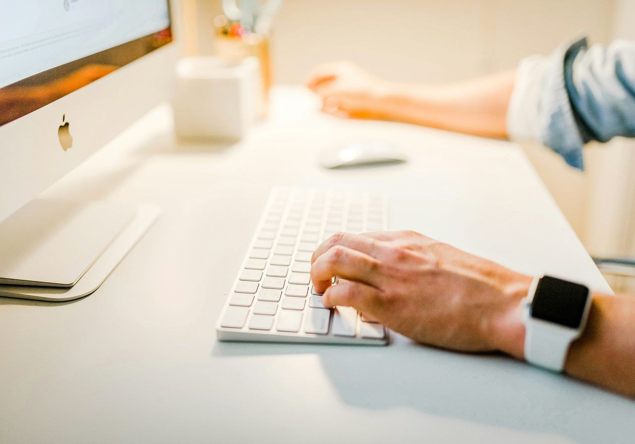 A person typing on a computer keyboard, focused on their work in a well-lit office environment.