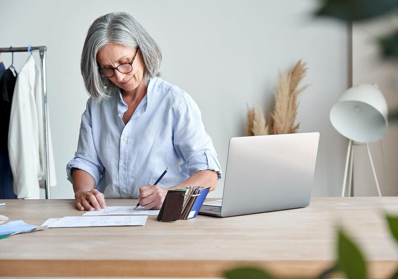 A woman sits at a desk, writing on a piece of paper with a focused expression.