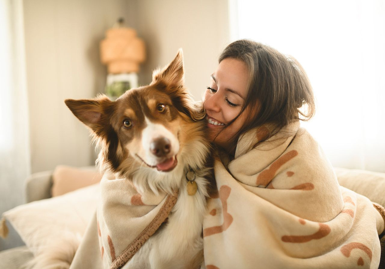 A woman with a blanket is hugging her dog