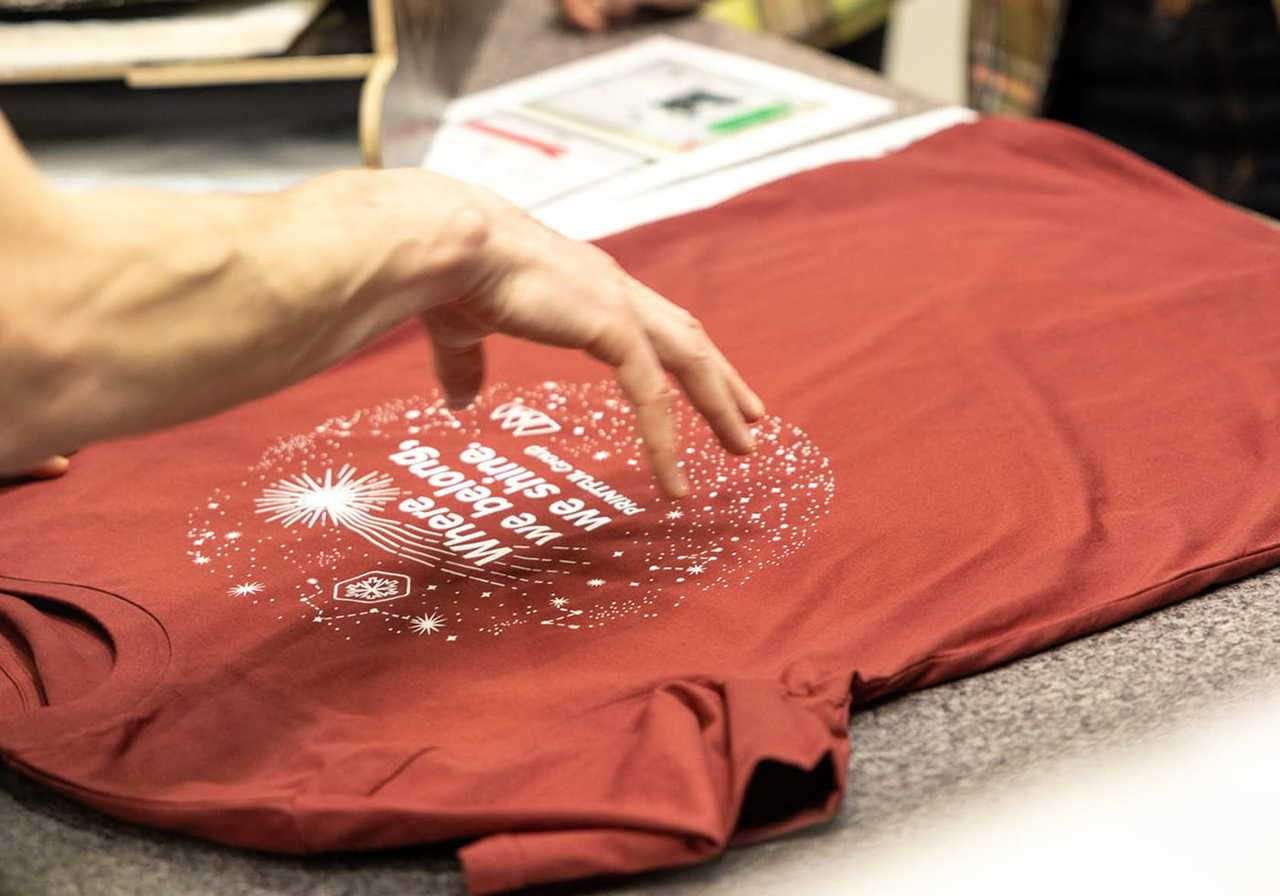 A hand reaching out to touch a red t-shirt with a circular white design that says 