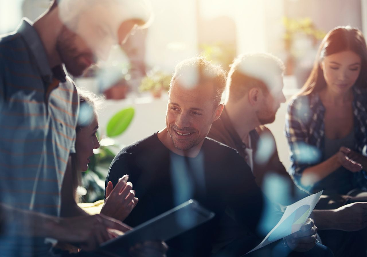 A diverse group of people gathered around a table, collaborating with a laptop in the center.