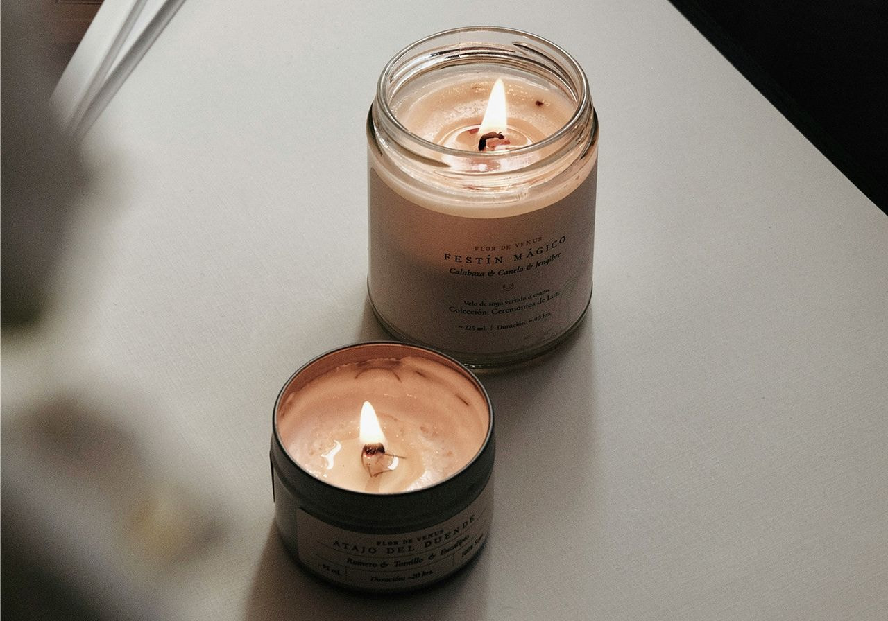 Two lit candles placed side by side on a wooden table, casting a warm glow in the surrounding area.