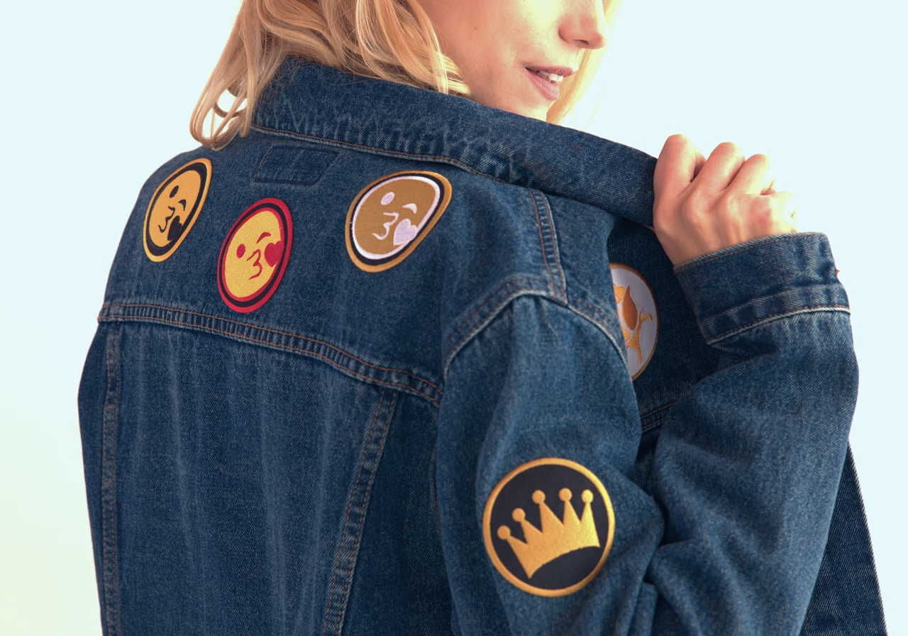 A woman wearing a denim jacket with multiple embroidery patches on the back.
