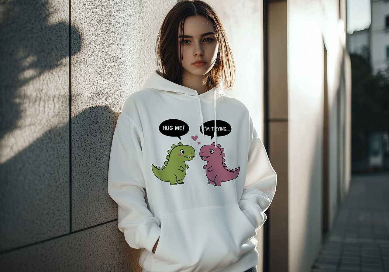 A young woman wearing a white hoodie with a cartoon design of two dinosaurs, one green and one pink, trying to hug.