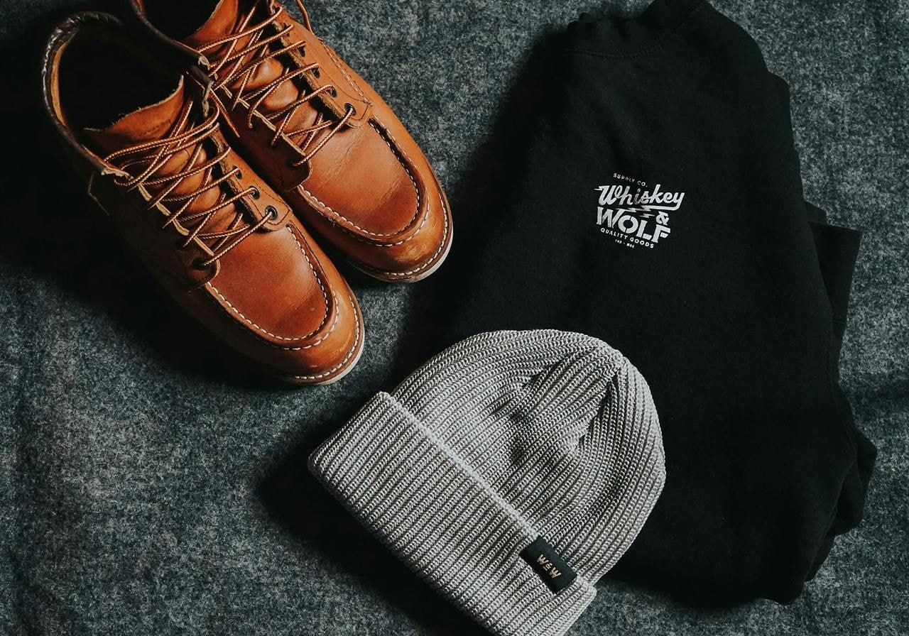 A sweatshirt, hat and a pair of shoes on top of a grey cloth.