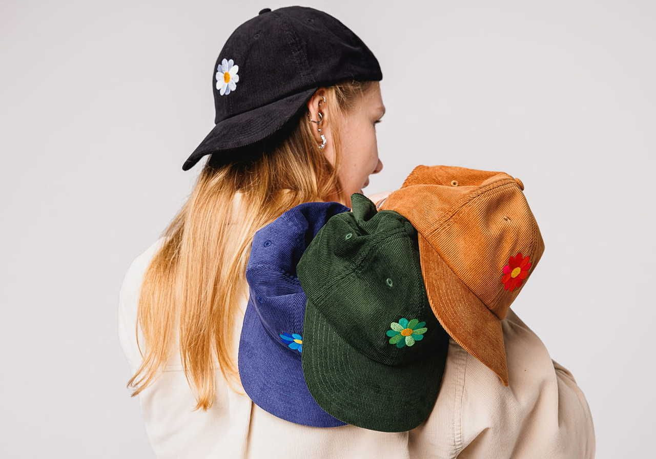 A backshot of a woman wearing and holding multiple caps with embroidered logos.