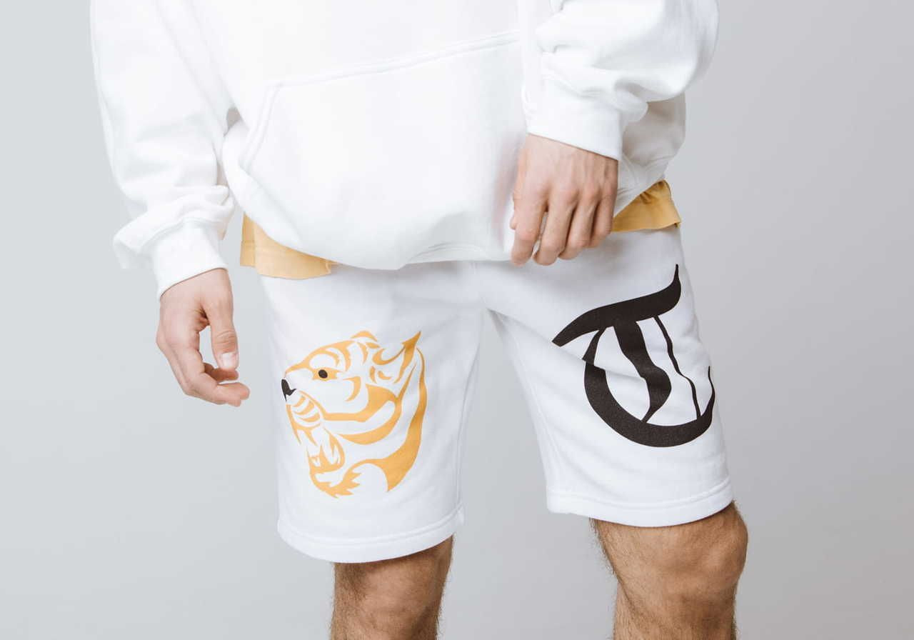 A person wearing a white hoodie and white shorts with a tiger design in orange on one side and a black logo on the other.