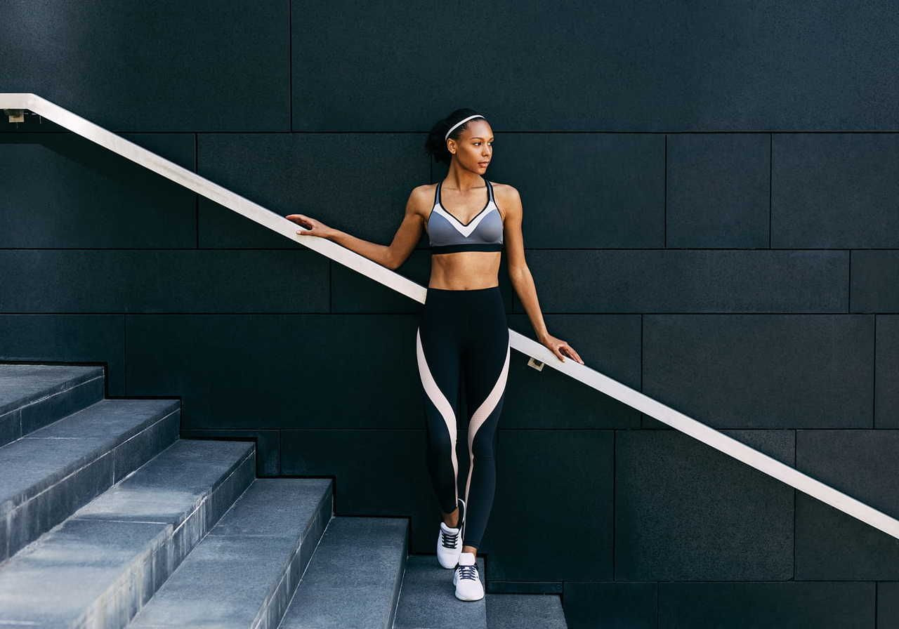 A woman in athletic wear leaning against a railing while standing on a staircase.