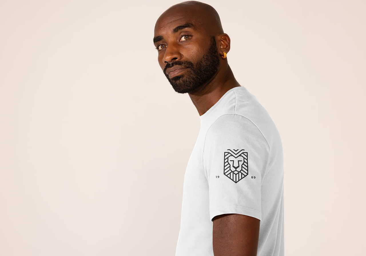 Man in a white t-shirt with a lion logo on the sleeve, looking confidently at the camera against a neutral background.