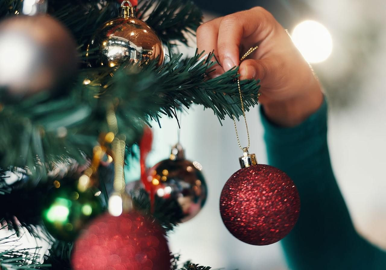 A person holds a red ornament while decorating a Christmas tree.
