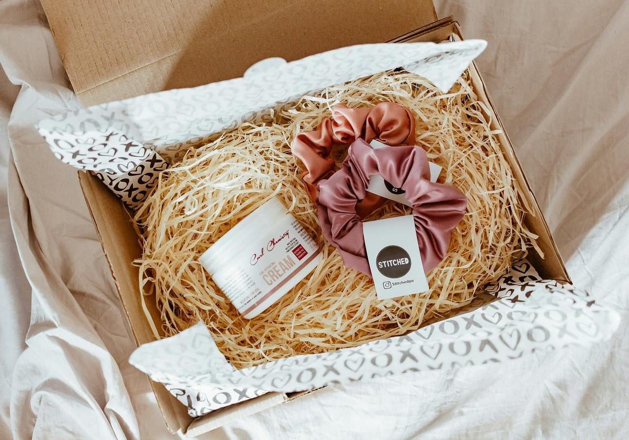 A subscription box containing a pair of colorful hair scrunchies and a cozy pair of socks, neatly arranged inside.