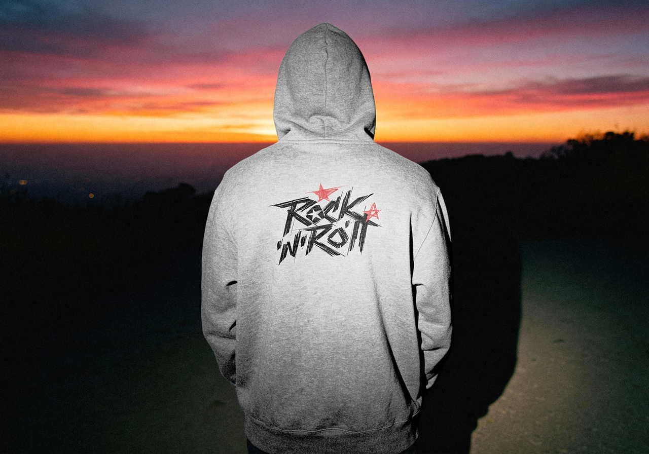 A person in a gray hoodie with "Rock 'N' Roll" text stands against a vivid sunset.