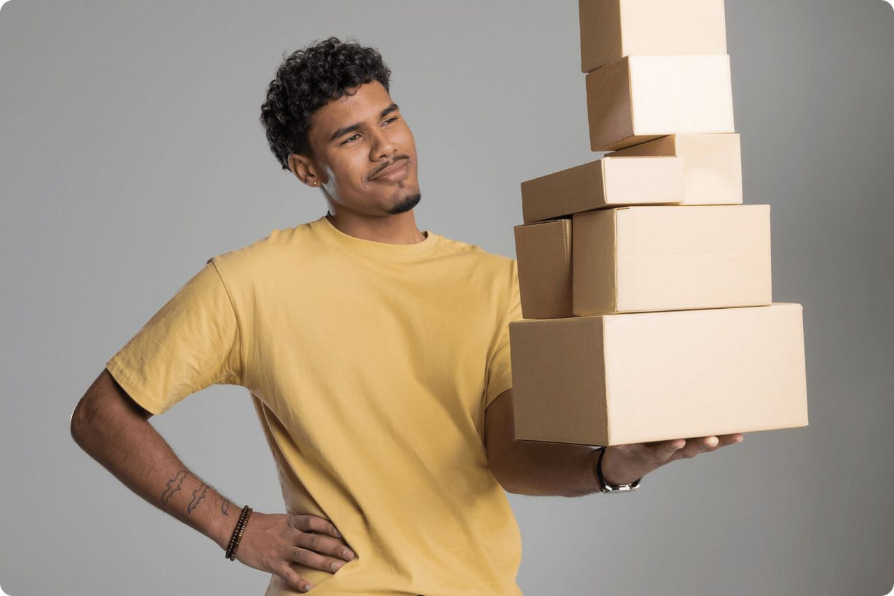 A man stands holding a tall stack of boxes, demonstrating strength and balance in a well-lit environment.