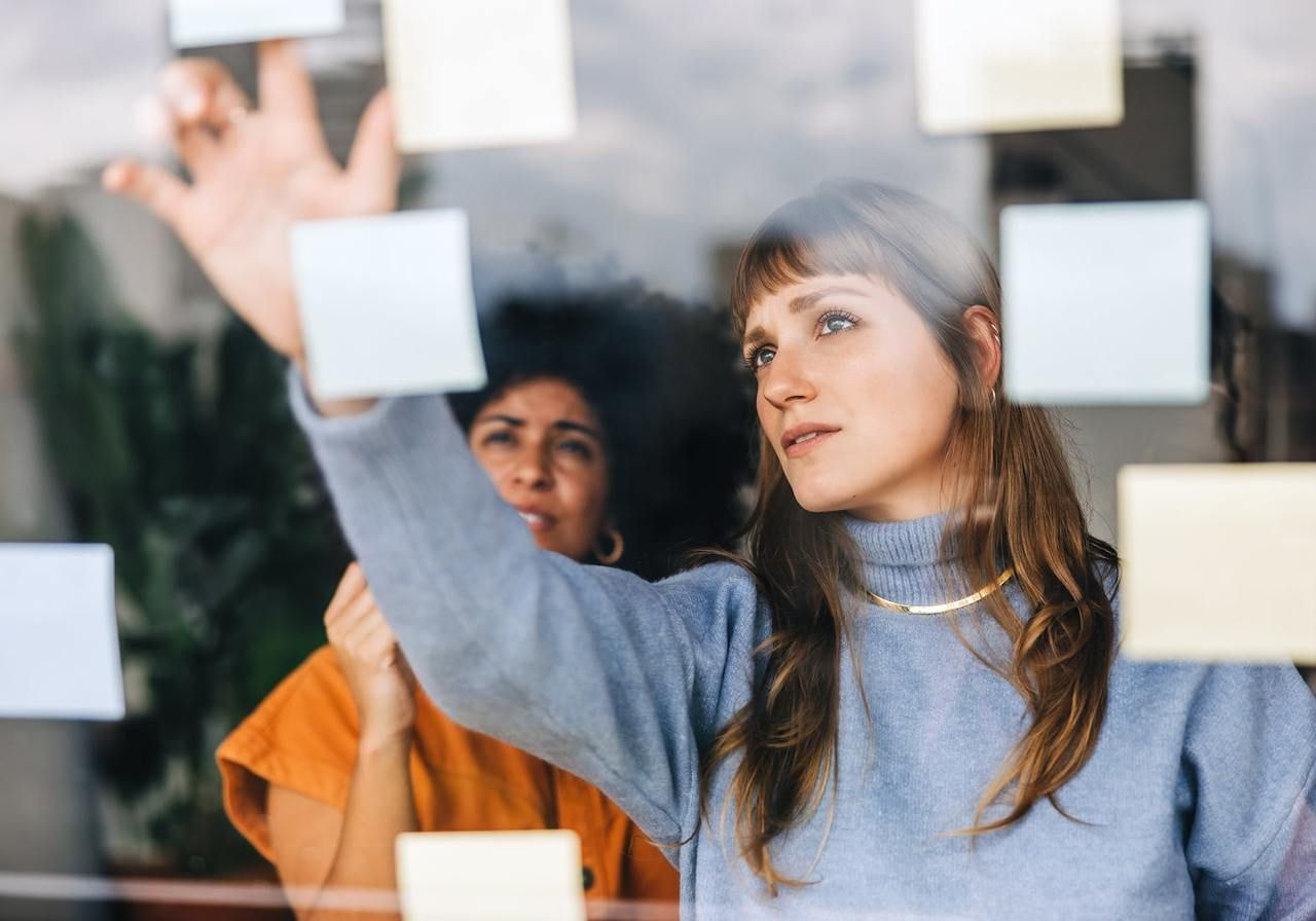 A woman is putting sticking notes on a glass as a process of brainstorming.