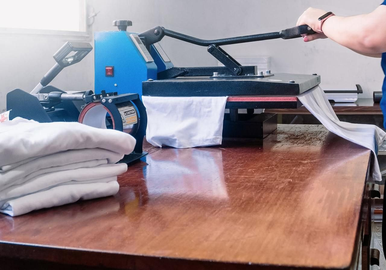 A man operates a machine to produce shirts in a workshop setting.