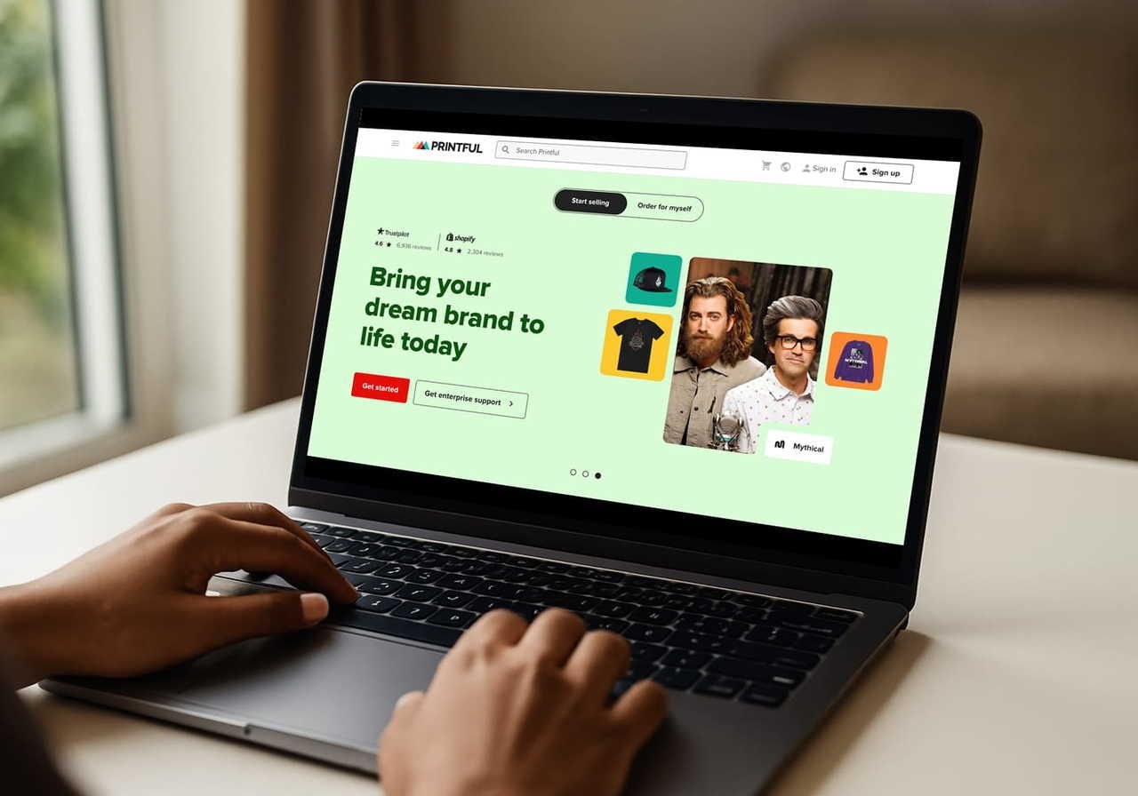 A person is using a laptop with Printful’s homepage on the screen, while sitting at a desk.