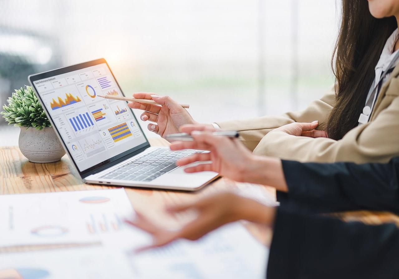 Close-up of two people in business attire analyzing colorful charts on a laptop. Hands are pointing at the screen.