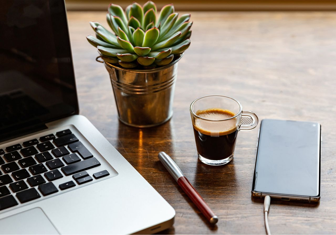 A laptop, a cup of coffee, and a small plant arranged on a wooden table, creating a cozy workspace atmosphere.