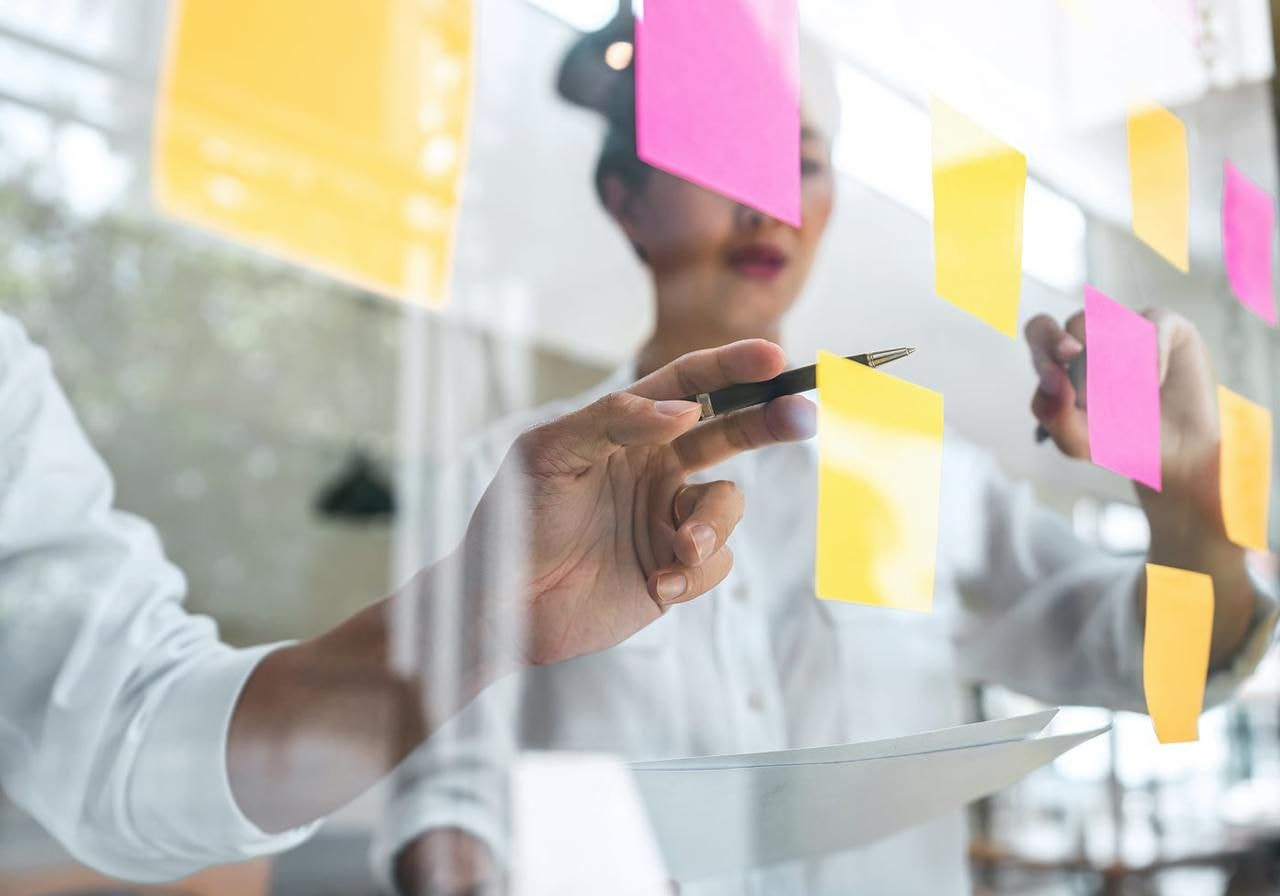 A man and woman are collaborating, writing ideas on colorful sticky notes at a table.
