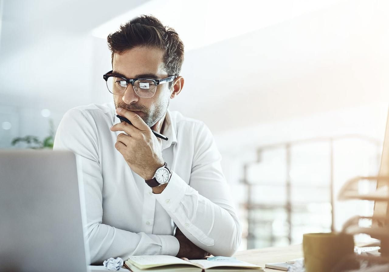A man in glasses is sitting at a desk and reading about AI fashion trends on a laptop.