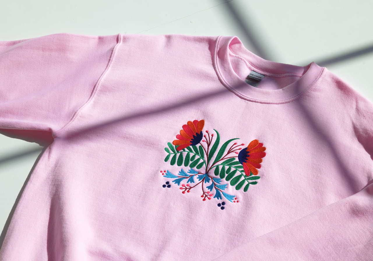A pink sweatshirt with a floral embroidered logo in the center.