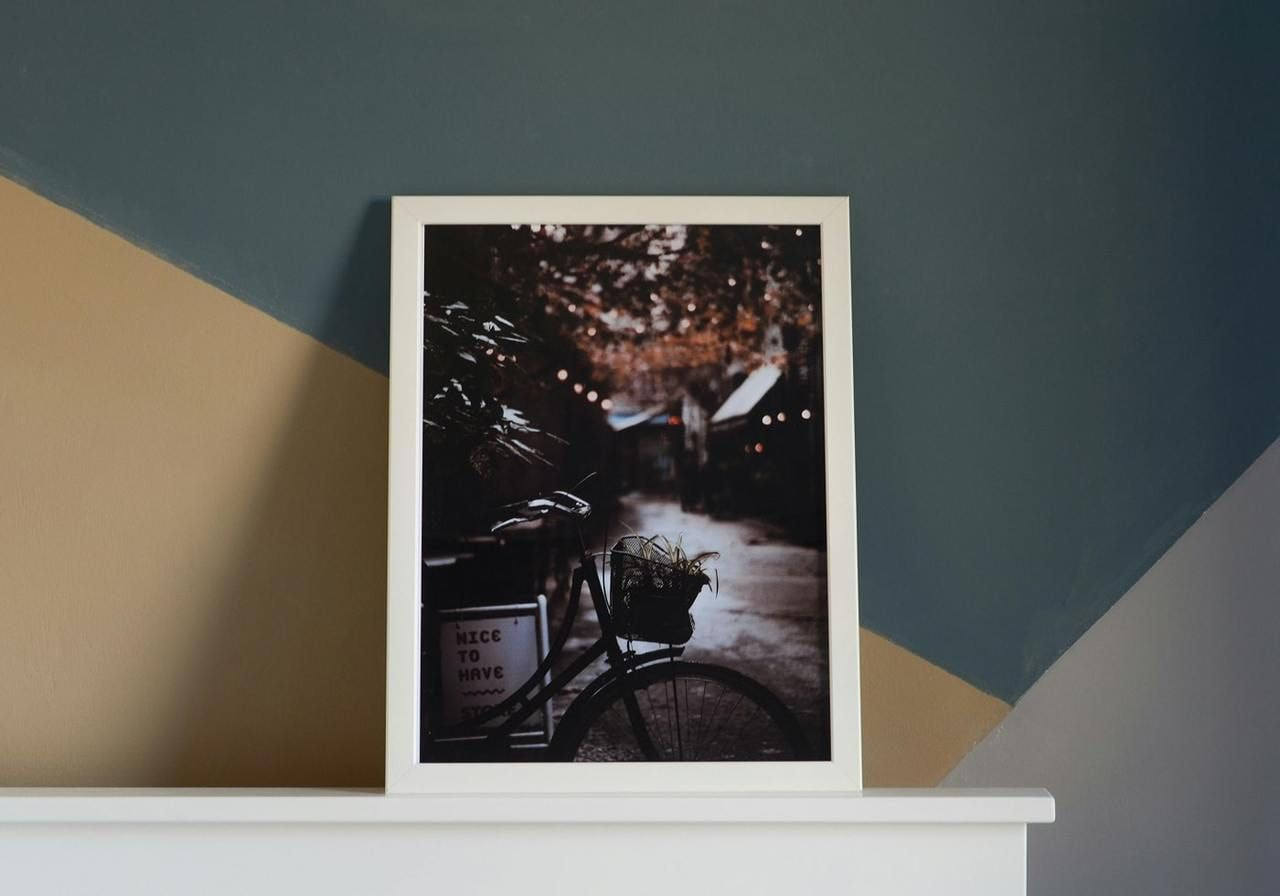 A framed metal print of a picture of a street standing above a fireplace.
