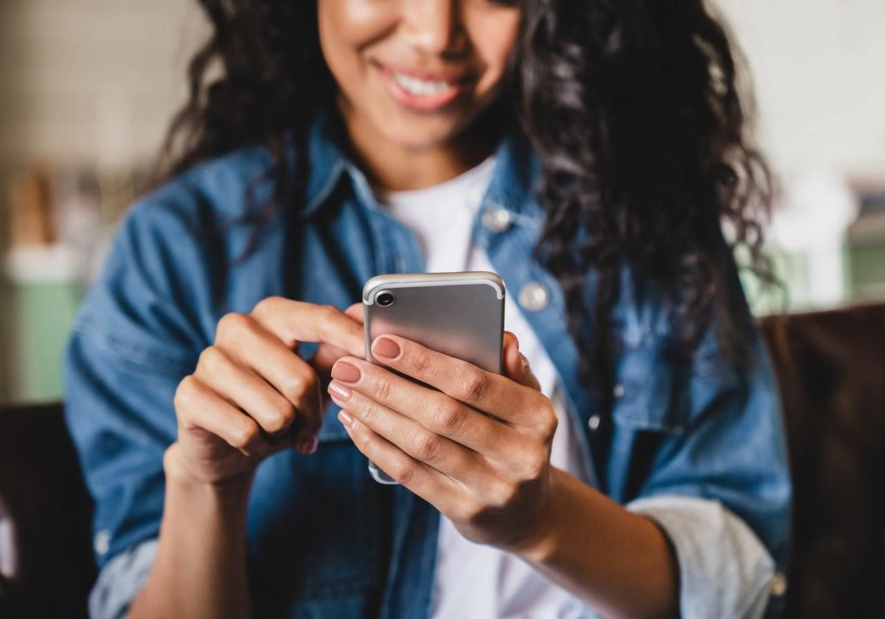 A smiling woman in a denim jacket is using a smartphone.