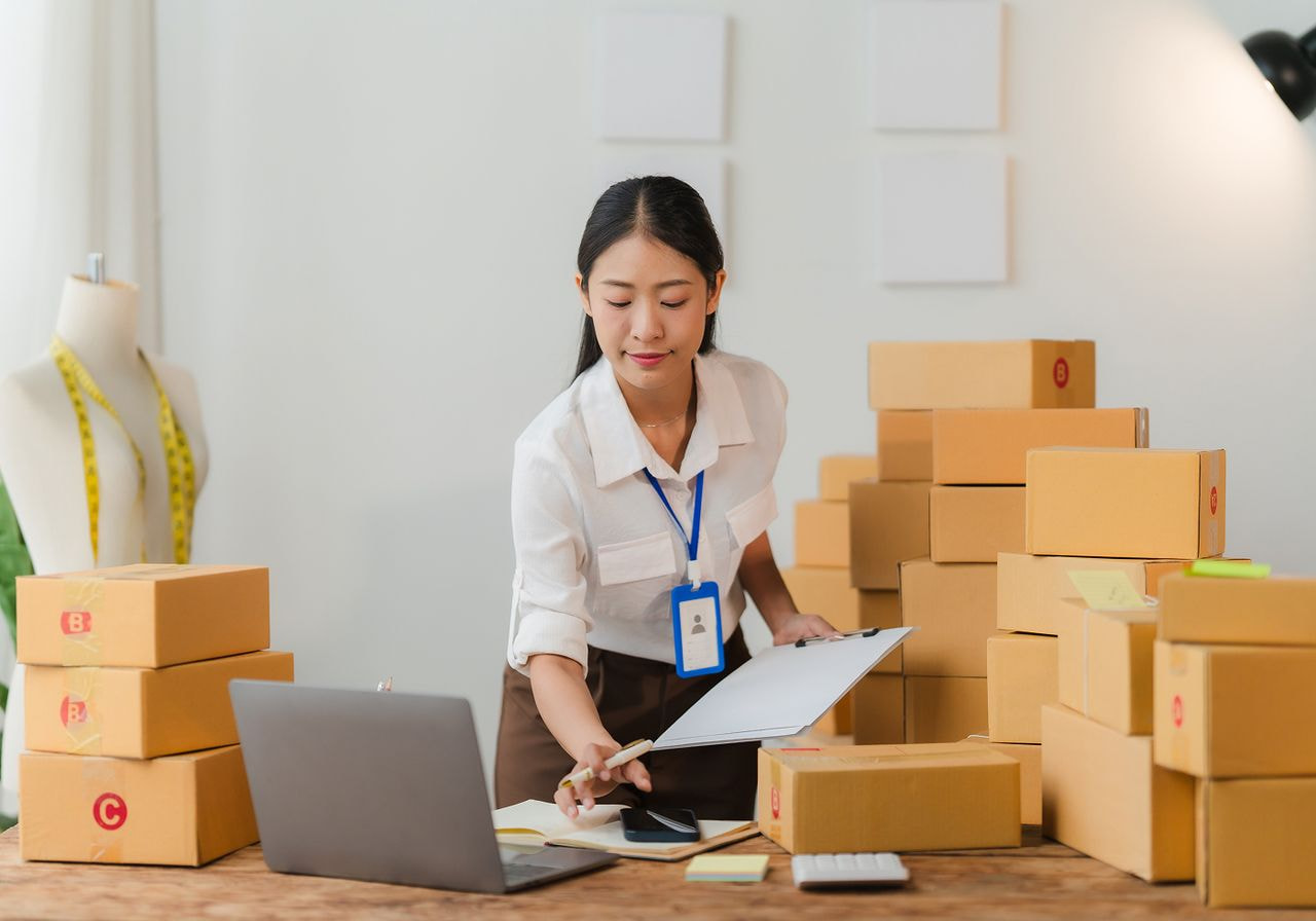 A woman works on a laptop while reviewing notes on a clipboard, focused and engaged in her task.