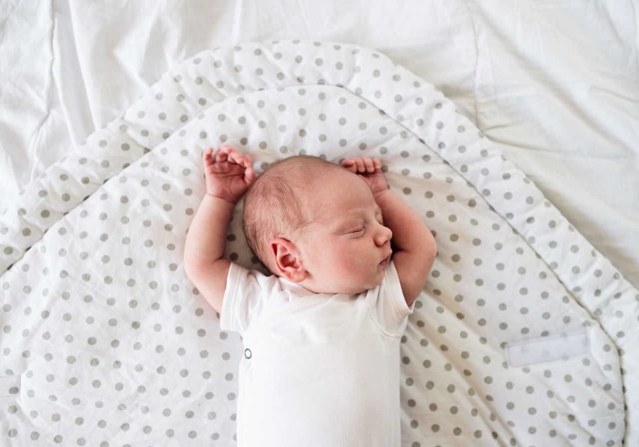 A sleeping newborn baby lying on a patterned blanket with arms raised.