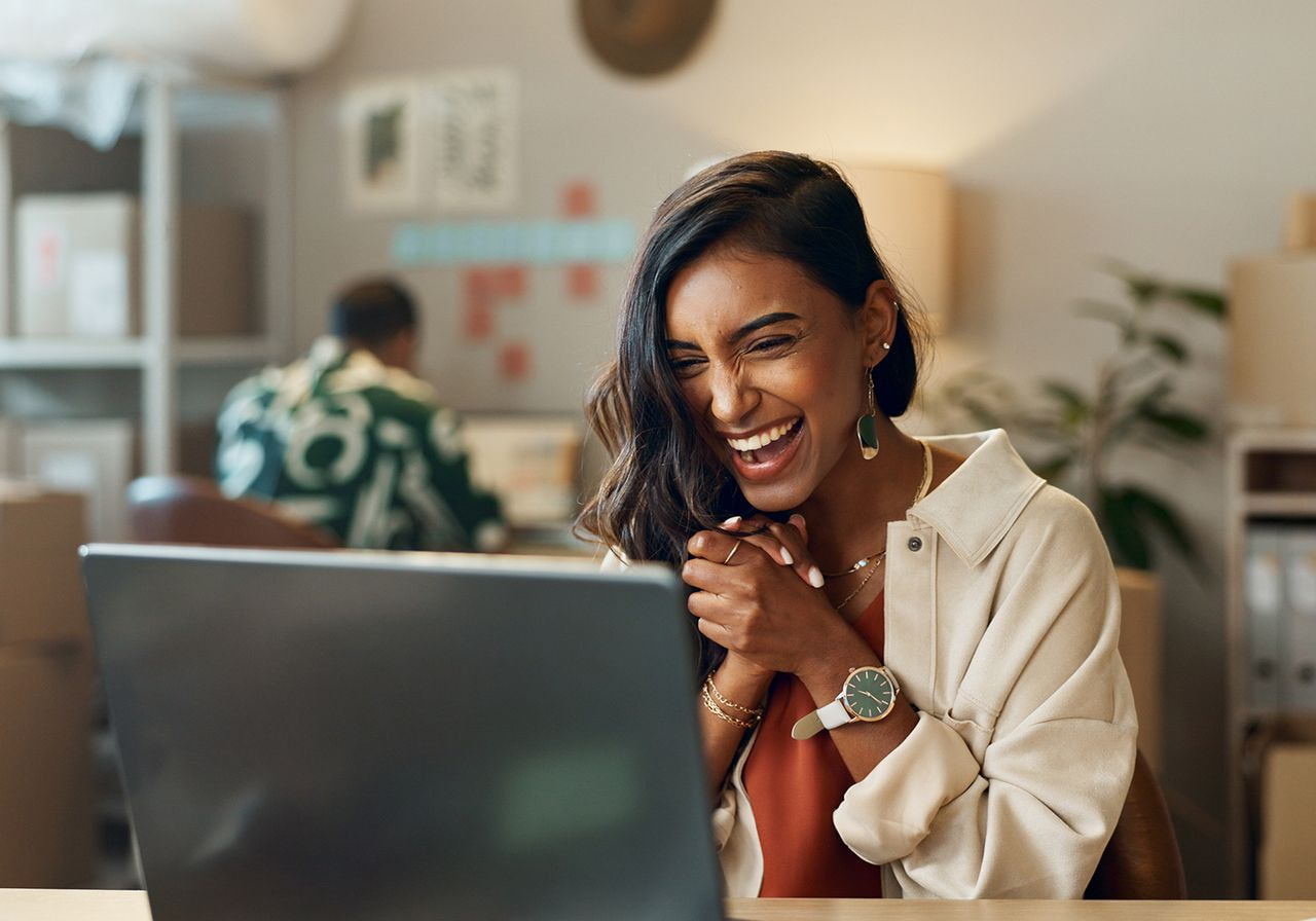 A woman is sitting happily in front of a computer