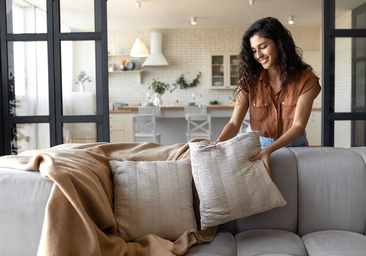 A woman arranging decorative pillows on a couch in a cozy living room setting.