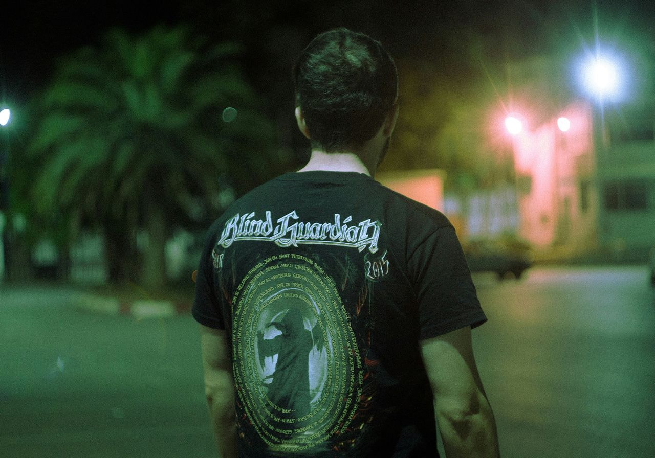 Man wearing a "Blind Guardian" shirt stands in a dimly lit urban setting.