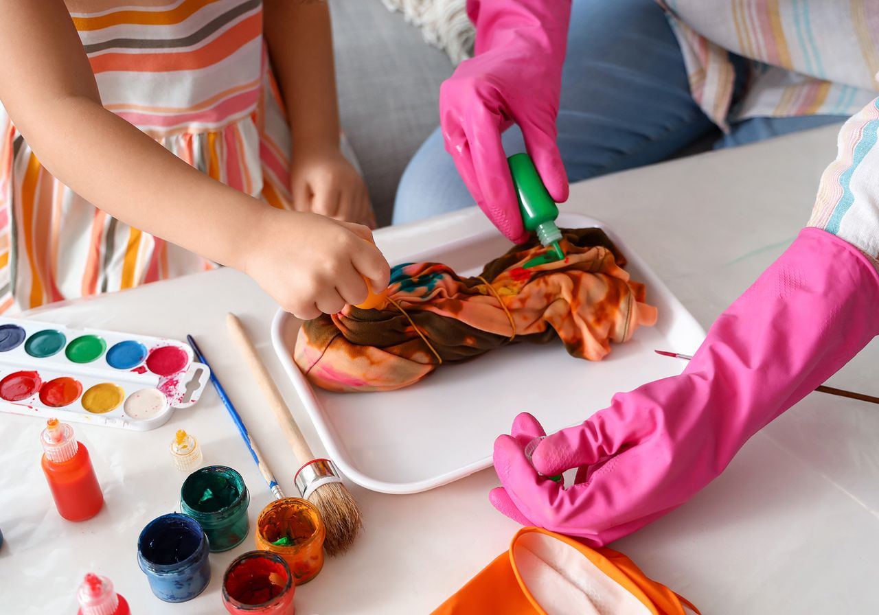 Child and adult hands create tie-dye art.