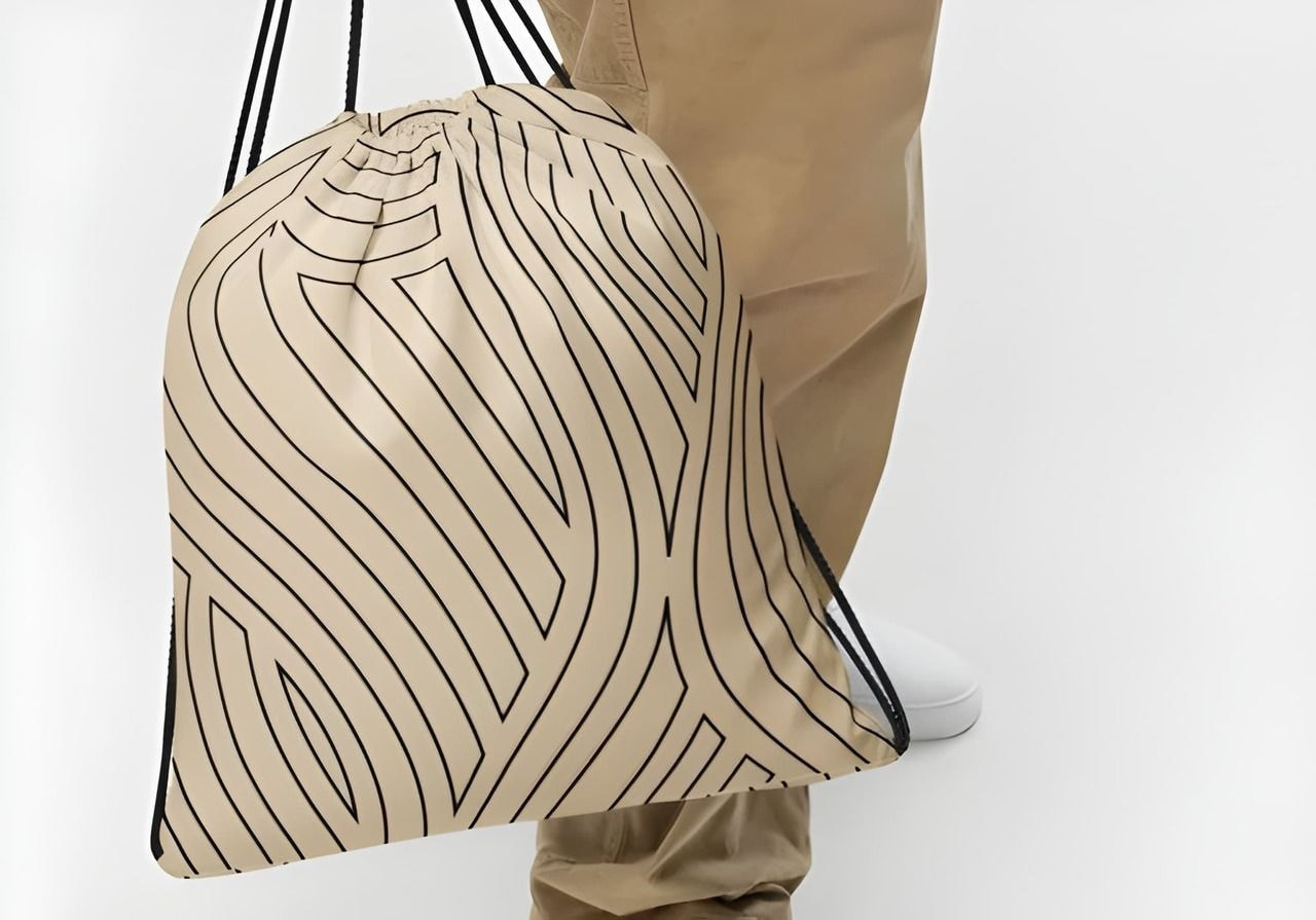Beige drawstring bag with black wavy lines, worn by a man in tan pants and white shoes against a light background.